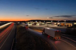 Semi trucks taking a highway exit at dusk toward a truck stop, tire shop and repair shop